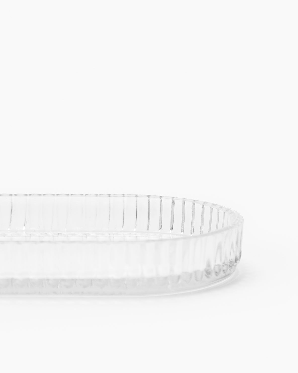 A clear oval tray from the Stein Glass Collection, featuring vertical ridges, is partially shown against a white background. This elegant blown glass piece is ideal for bathroom countertops.