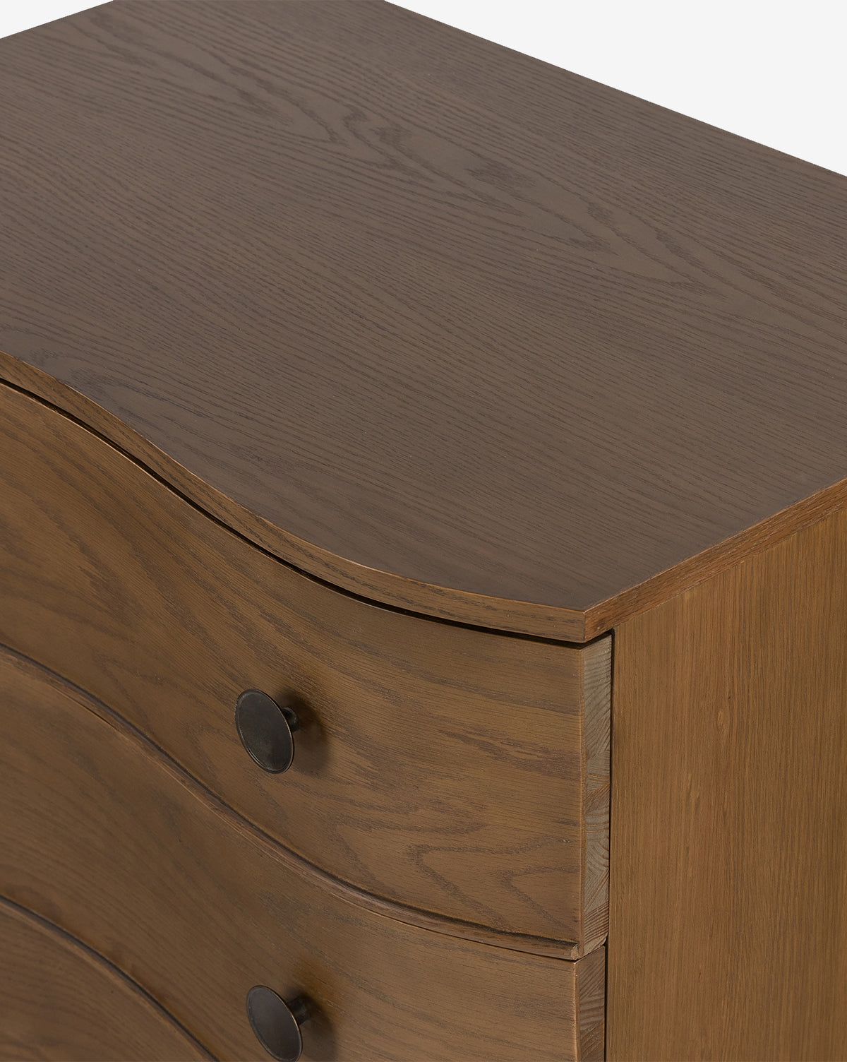 A close-up of the Strasburg Nightstand shows its natural wood finish, curved drawer fronts, and round dark metal knobs—an antique-inspired piece ideal for timeless bedroom style, by McGee & Co.