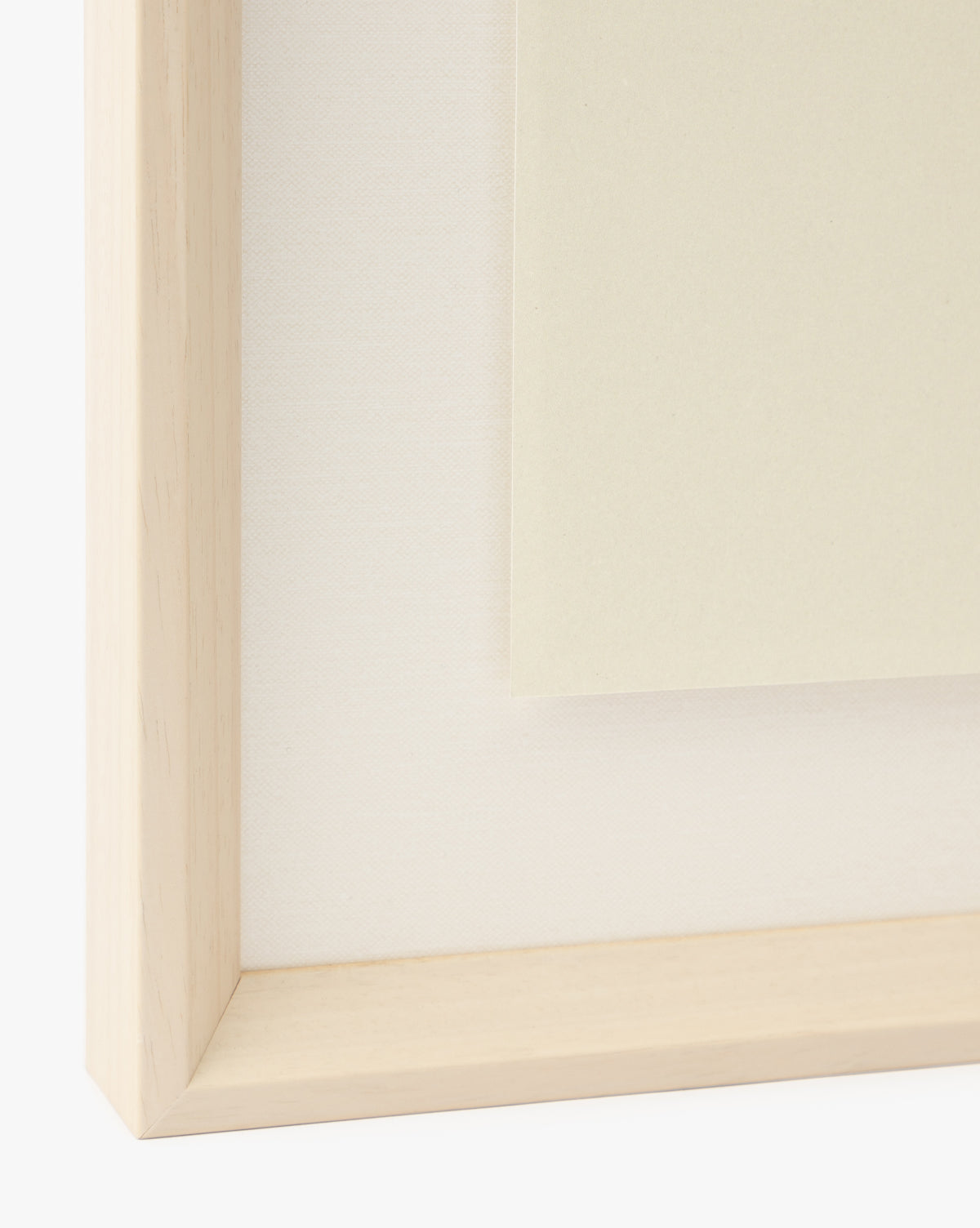 Close-up of the corner of a light wooden frame with a white mat featuring “Strawberry Collage”—a giclee print with cream-toned art. This minimalist design adds subtle charm to any children’s room, by McGee & Co.