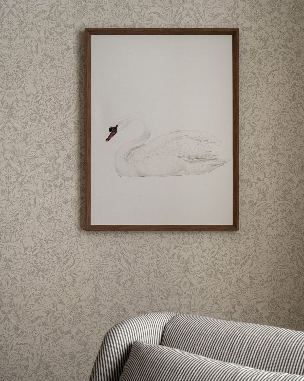 The Neutral Swan giclee print hangs framed on a patterned beige wallpapered wall above a striped upholstered sofa.