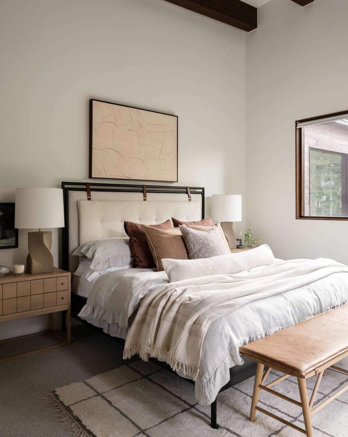 A cozy, modern bedroom features a neatly made bed with the Ruffle Linen Duvet Cover and neutral pillows. Two wooden nightstands with lamps, a bench at the foot of the bed, and large abstract artwork complete the inviting look.