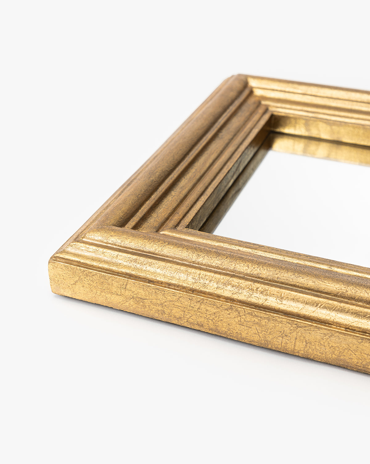 A close-up of the Suzanne Shelf Mirrors gold-finished frame with ridged detailing, shown against a plain white background, by McGee & Co.