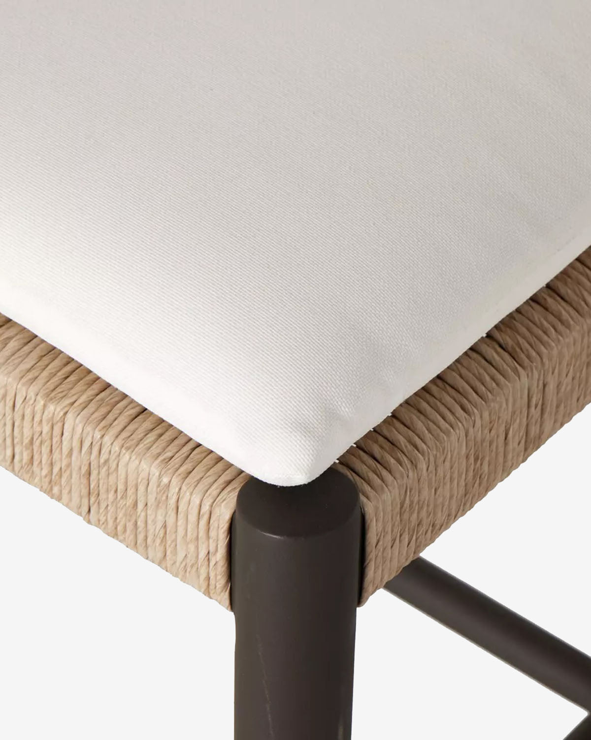 Close-up of the Tabitha Outdoor Dining Chair shows its black aluminum frame, woven wicker seat edge, and a removable white cushioned seat by McGee & Co.