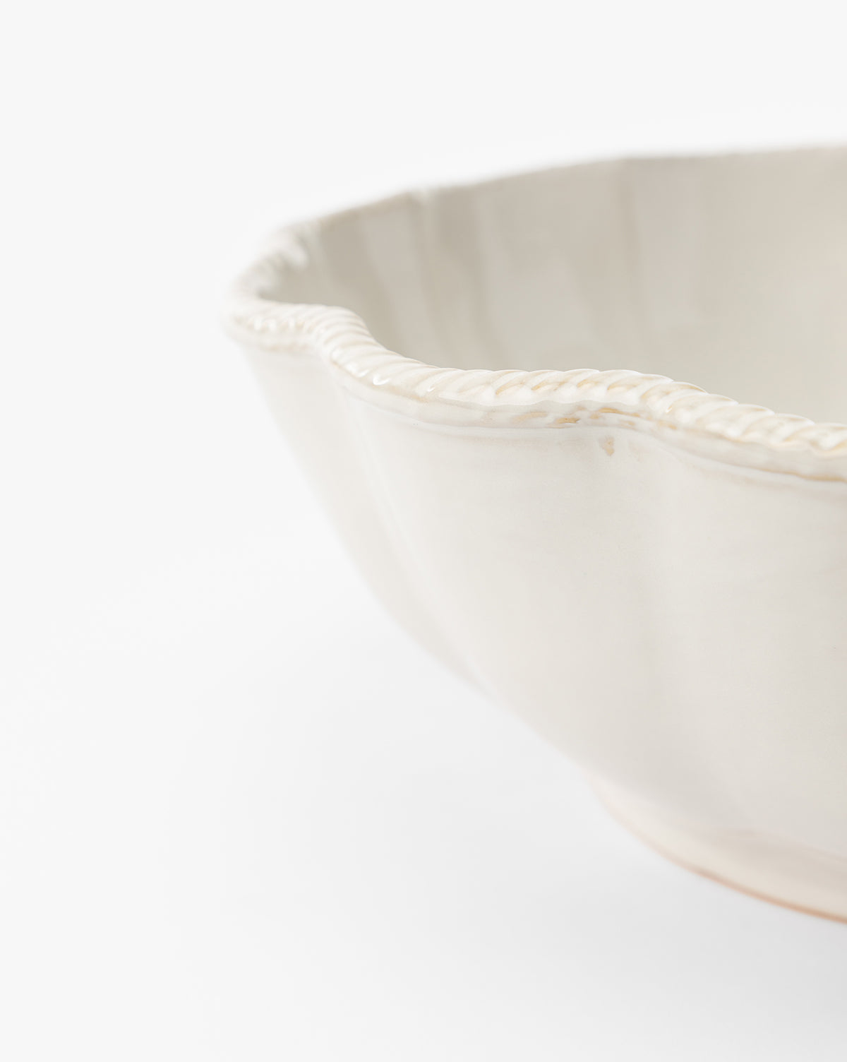 Close-up of the edge of the McGee & Co. x Loeffler Randall Tabitha Serving Bowl, featuring an ivory ceramic finish and a slightly scalloped rim, set against a plain white background, by McGee & Co.
