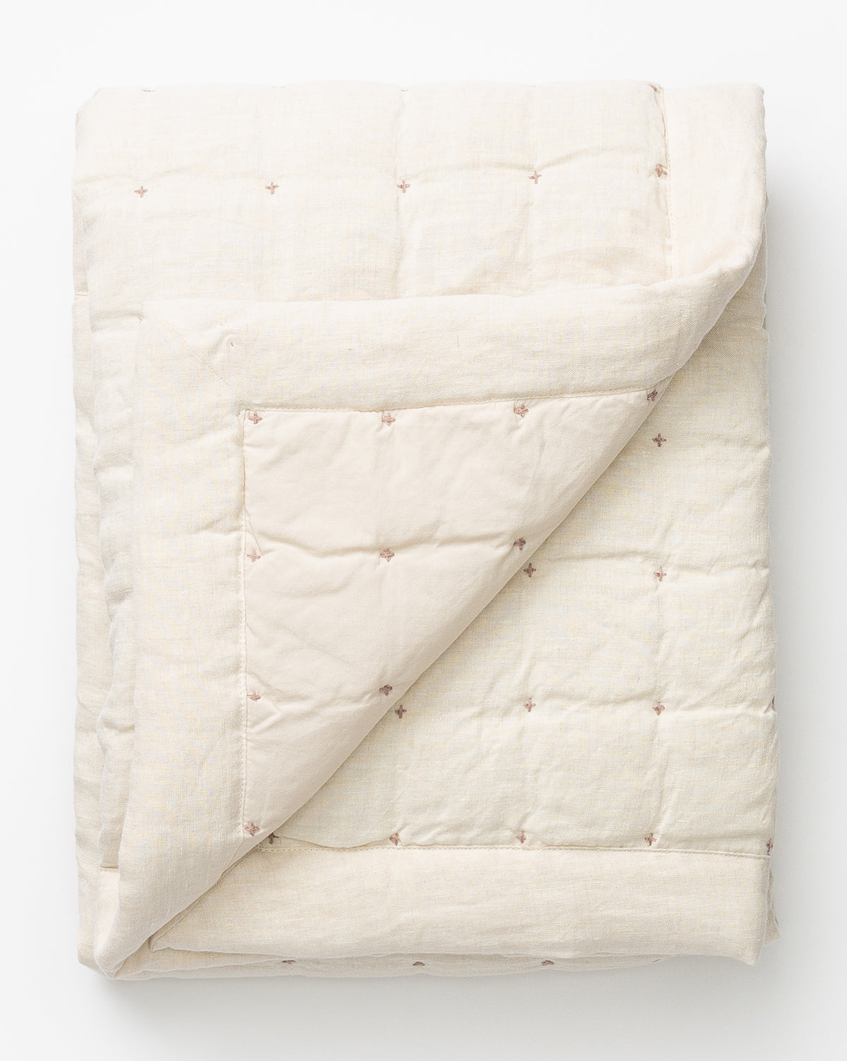 The Talcott Quilt, a cream-colored cotton piece with subtle stitched cross motifs, is neatly folded and displayed on a white background. One corner is turned over to reveal the inner side, highlighting its neutral palette.