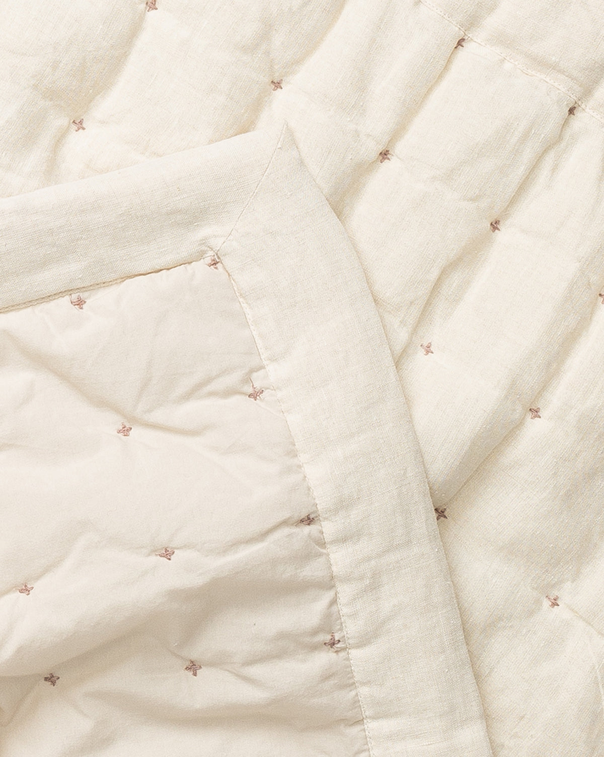 A close-up of the Talcott Quilt, crafted from cream-colored cotton with small, light brown embroidered stars. This softly textured quilt features a neutral palette and neat stitching for a refined look.