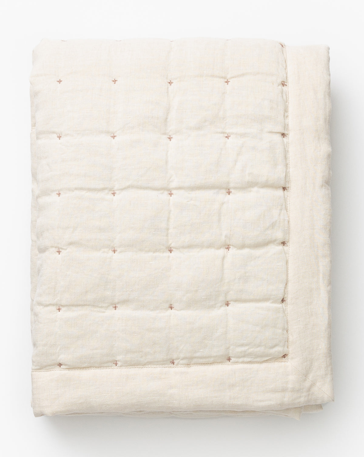 The Talcott Quilt is a folded, cream cotton quilt with a subtle grid pattern and small, evenly spaced brown stitched accents, shown on a white background—an ideal choice for any neutral quilt collection.