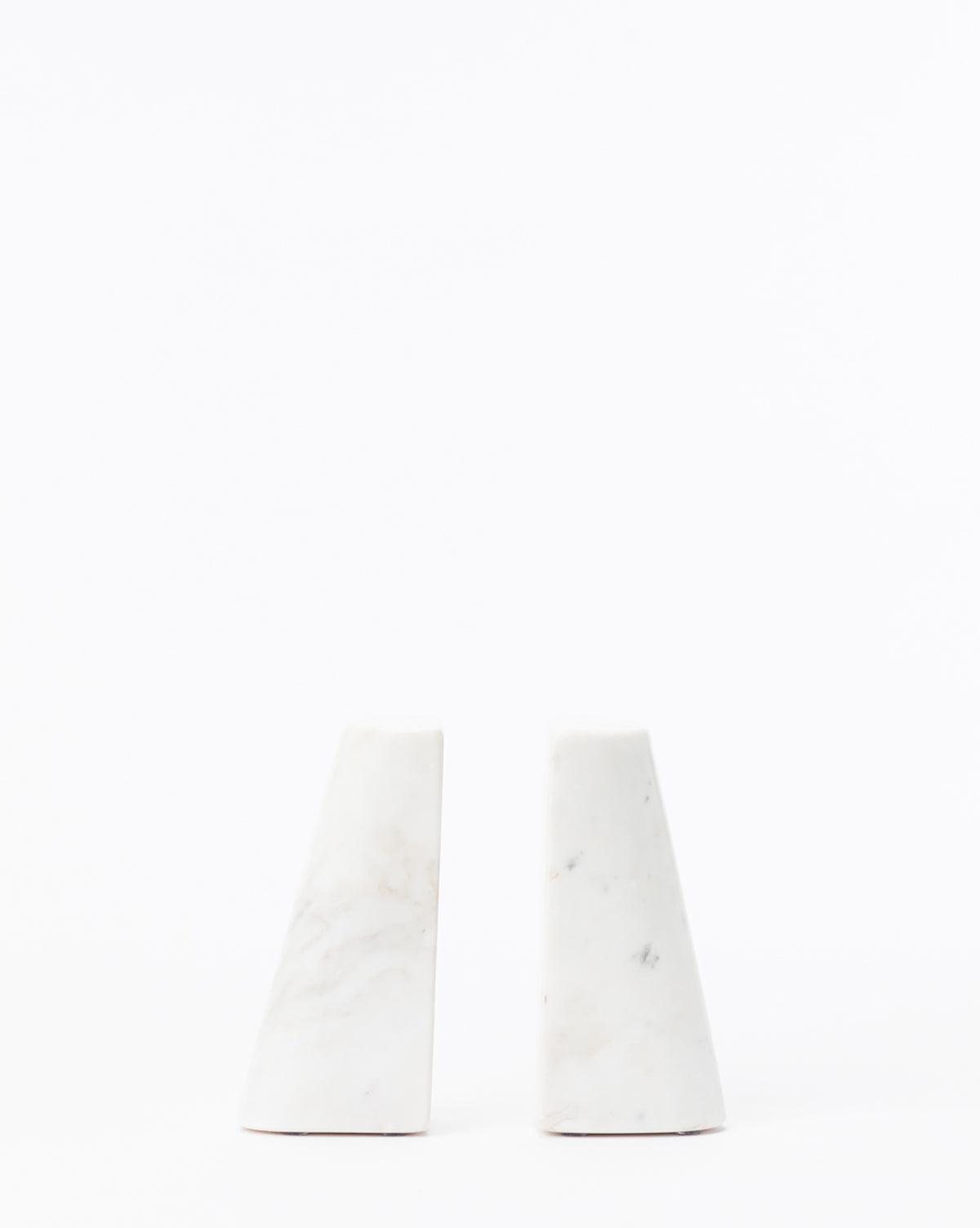 The Tapered Marble Bookends (Set of 2) feature a geometric, modern design in smooth white marble with subtle pattern variations, shown side by side against a plain white background.