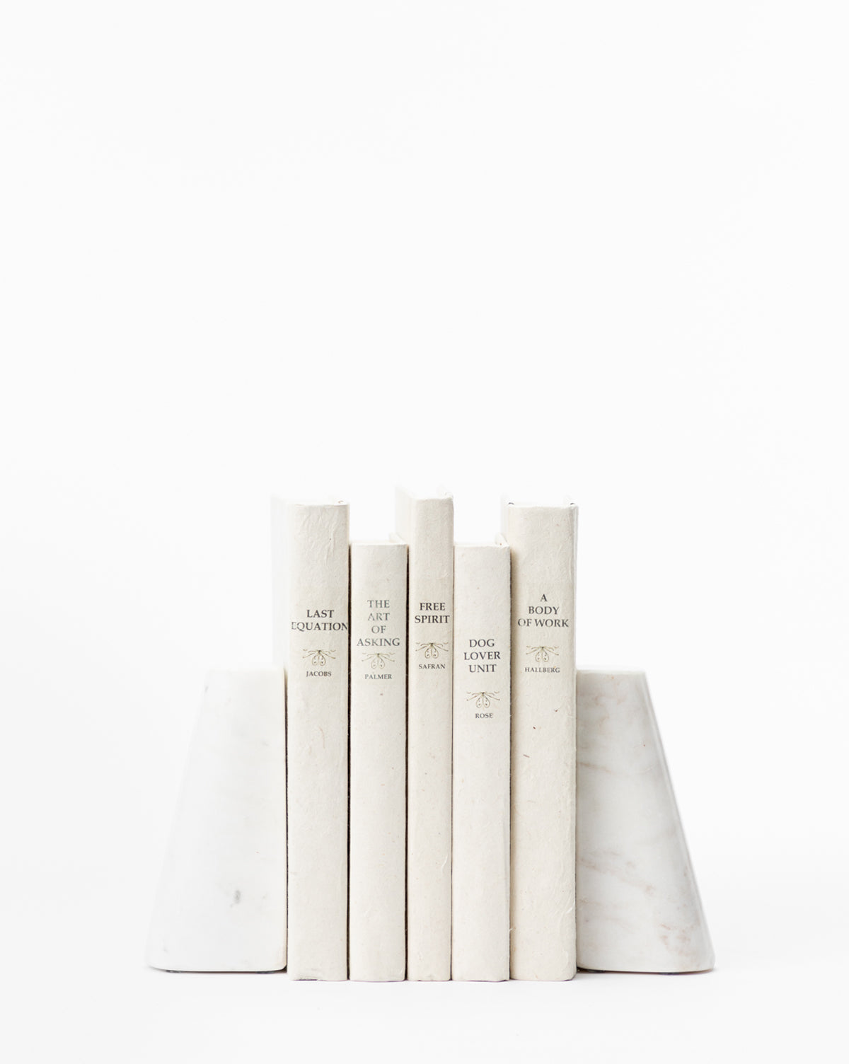 Five white books with minimalist covers stand upright between a Set of 2 Tapered Marble Bookends on a white background. Subtle, neutral spine fonts enhance the clean, elegant look of these marble bookends.