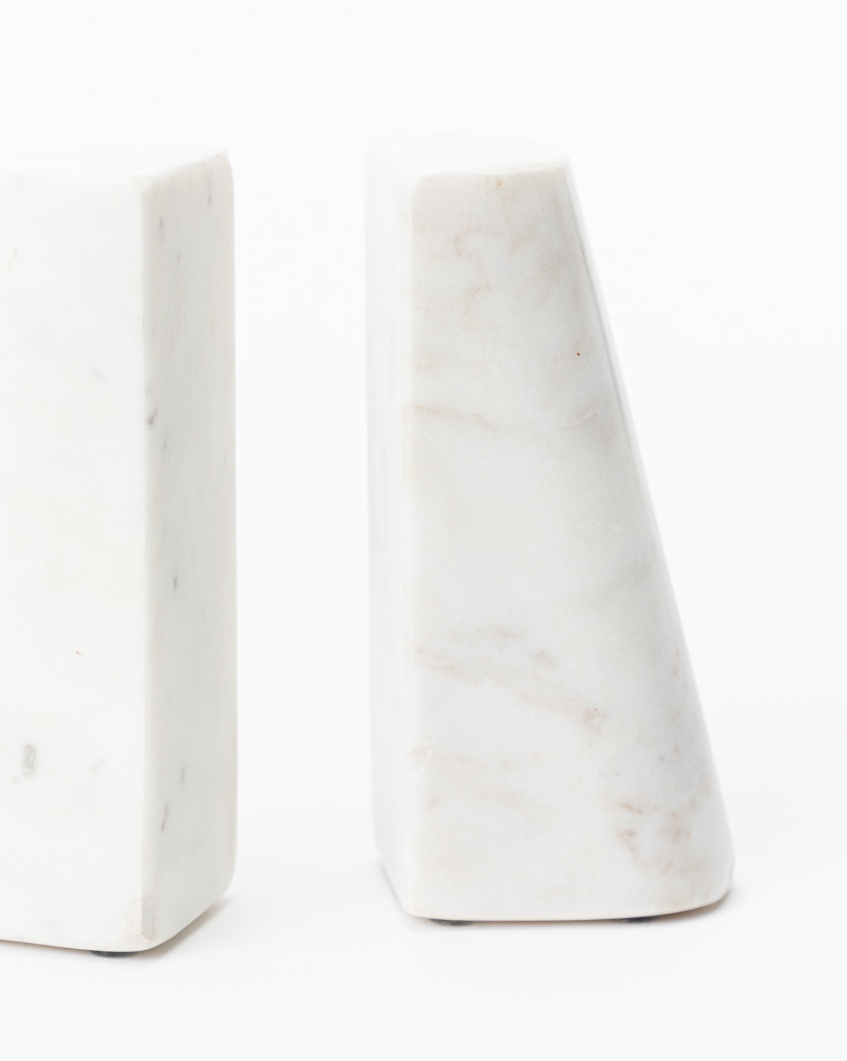The Tapered Marble Bookends (Set of 2) feature geometric, minimalist shapes in white marble with subtle grey veining, offering both function and style. Positioned against a plain white background, their smooth surfaces stand out.