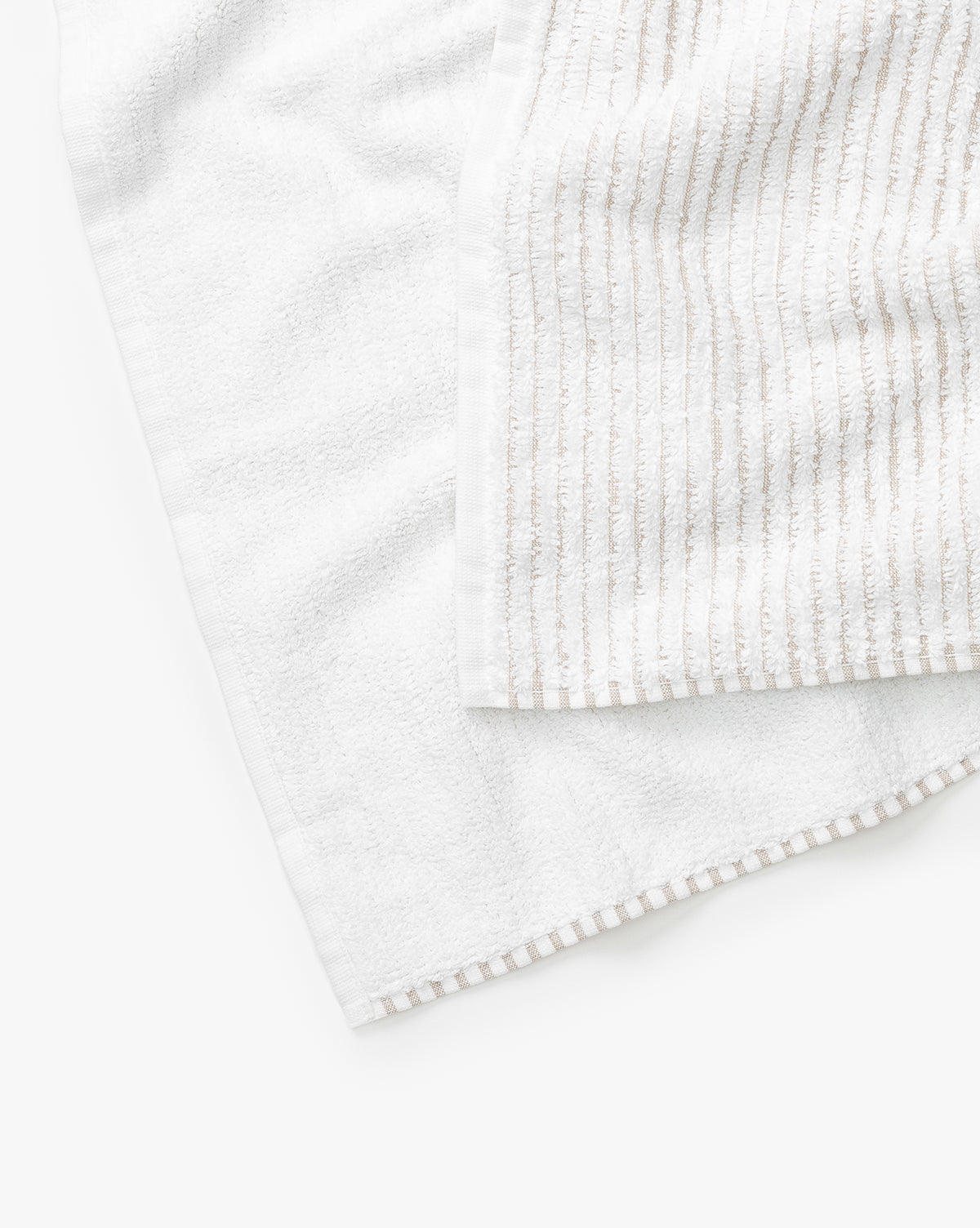 Two towels from the Taupe Striped Bath Collection are displayed overlapping: one features absorbent Aegean cotton with a striped, ribbed pattern, while the other has a plain texture. Both are neatly arranged on a white surface.