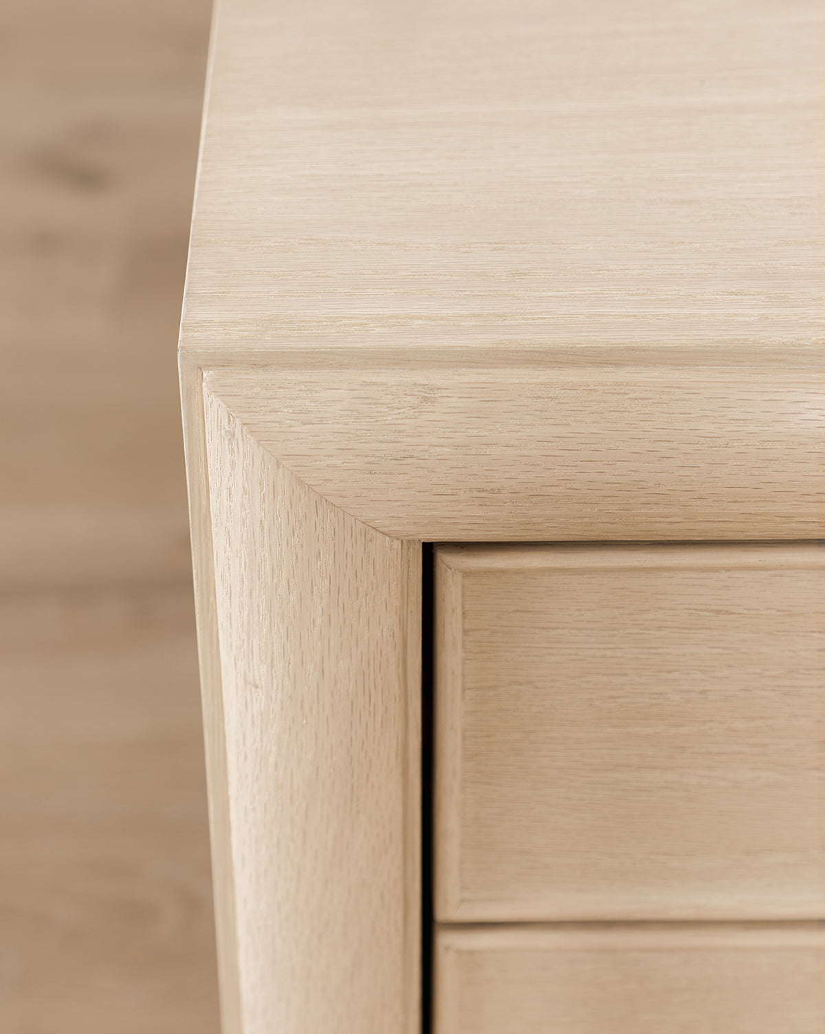 Close-up of the Tellerbeck Nightstand corner, displaying smooth, clean lines and natural wood grain on its bleached oak finish. Two drawer fronts and the top are partially visible—ideal for refined bedroom decor, by McGee & Co.