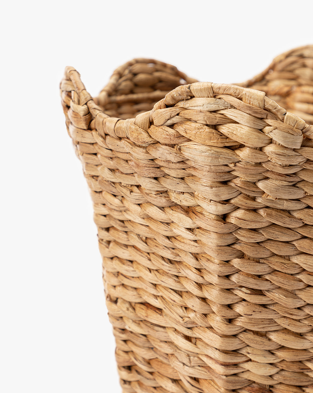 Close-up of the Tenley Woven Waste Bin, crafted from natural light brown water hyacinth fibers with a distinctive scalloped rim, shown against a plain white background.