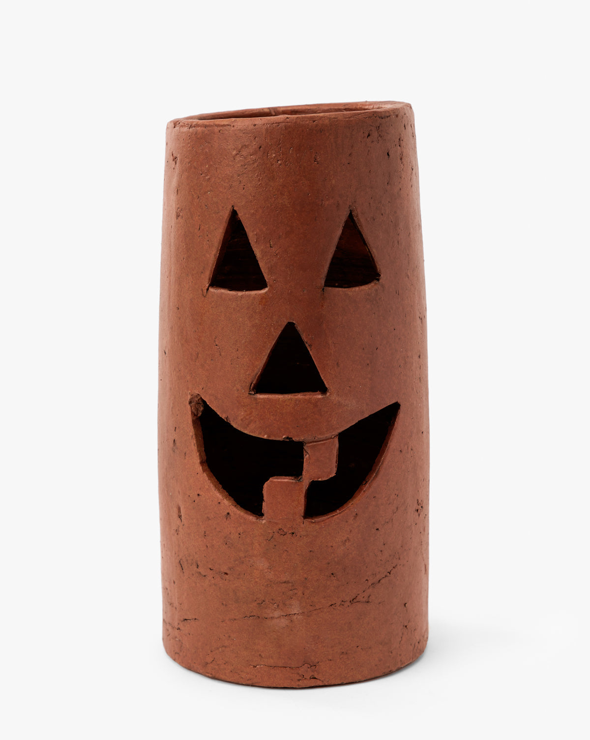 The Terracotta Jack-O Lantern Hurricane is a cylindrical, brown lantern with a carved face—triangular eyes, triangle nose, and a wide toothy smile. Its slightly rough surface and uneven top make it ideal for Halloween décor, by McGee & Co.