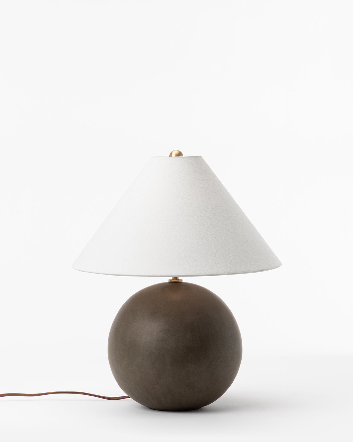 The Tess Ceramic Table Lamp features a round dark brown ceramic base and a wide conical white shade, set against a plain white background. A brown power cord extends from the base, by McGee & Co.