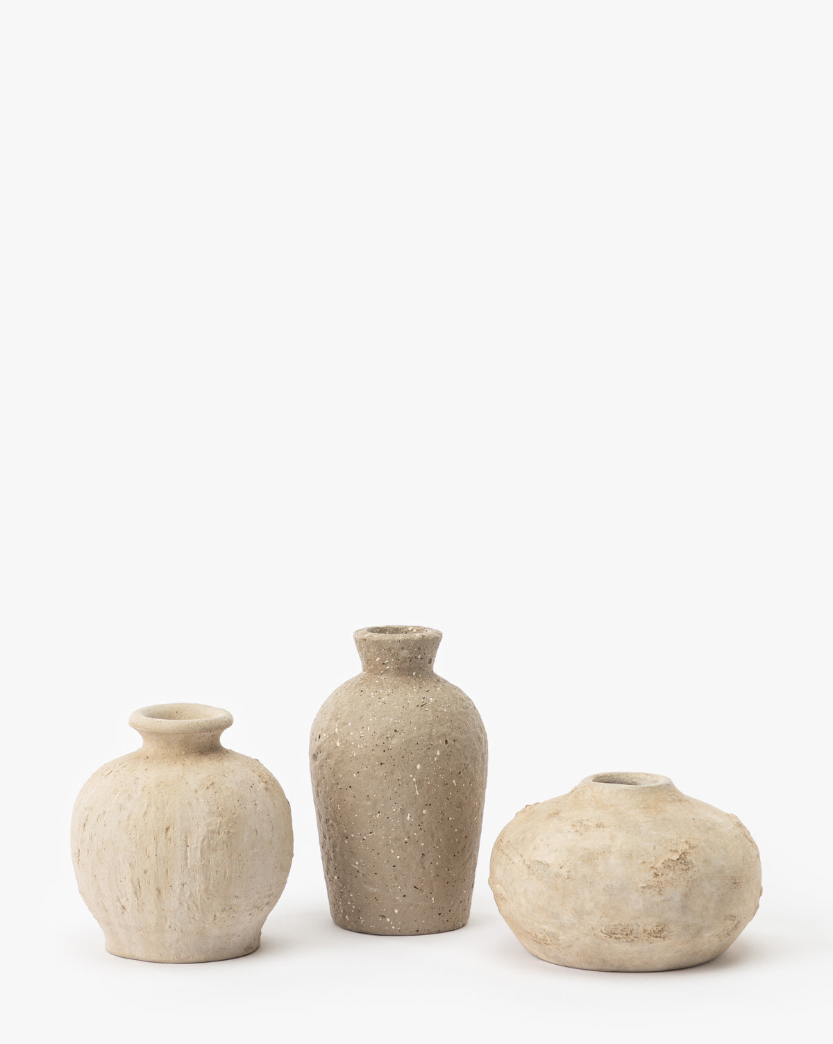 Three handcrafted Thalia Bud Vases (Set of 3), each with textured, neutral-toned terracotta finishes and unique shapes and sizes, are arranged side by side against a plain white background.
