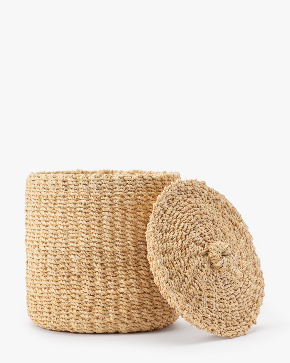 The Thalia Woven Canister, featuring a round abaca design and angled lid, is ideal for organic storage or as stylish bathroom counter decor. Shown against a white background.