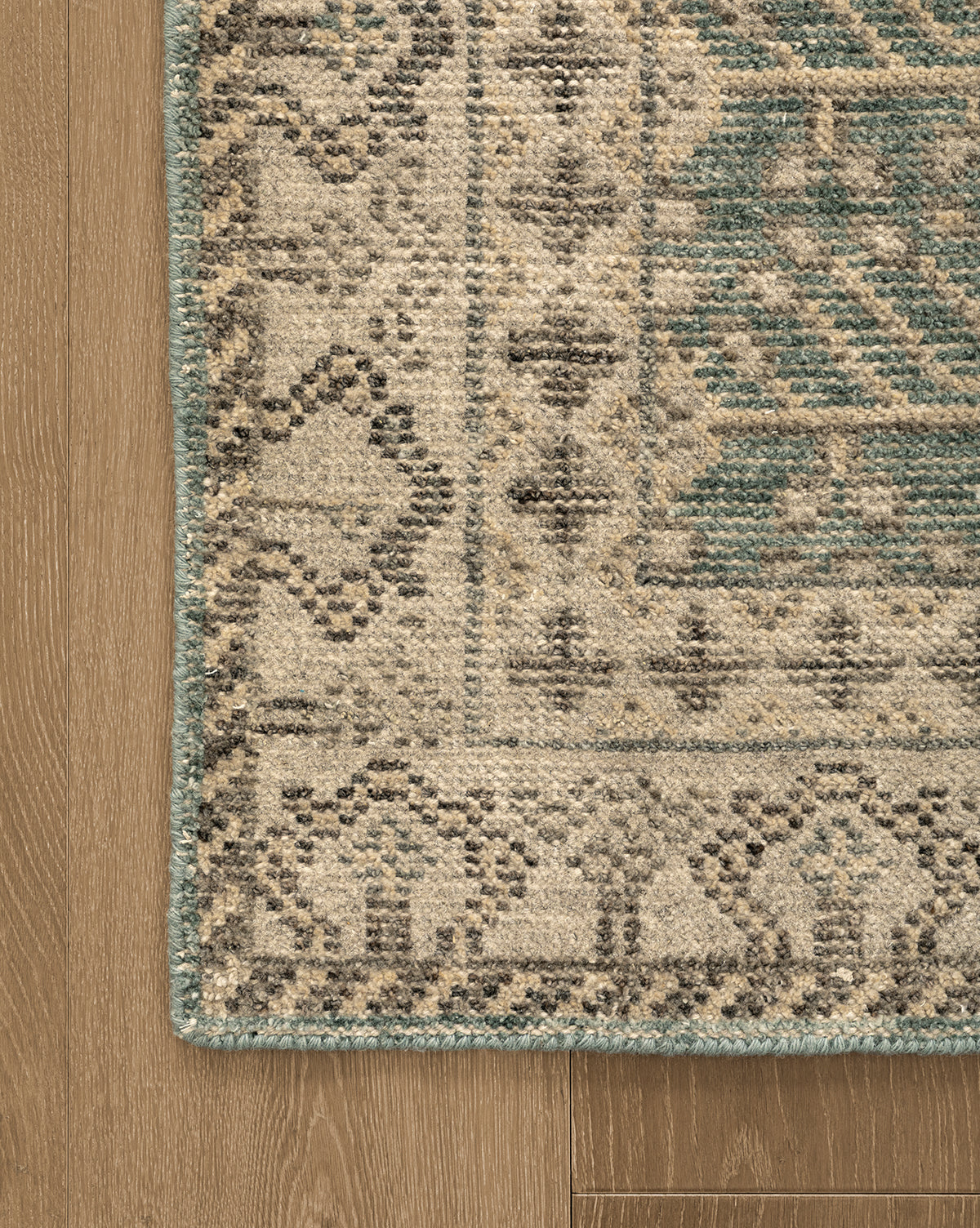 Corner of the Thames Hand-Knotted Rug with beige, green, and dark gray geometric designs on light brown wood flooring—a timeless addition to luxury home decor, by McGee & Co.
