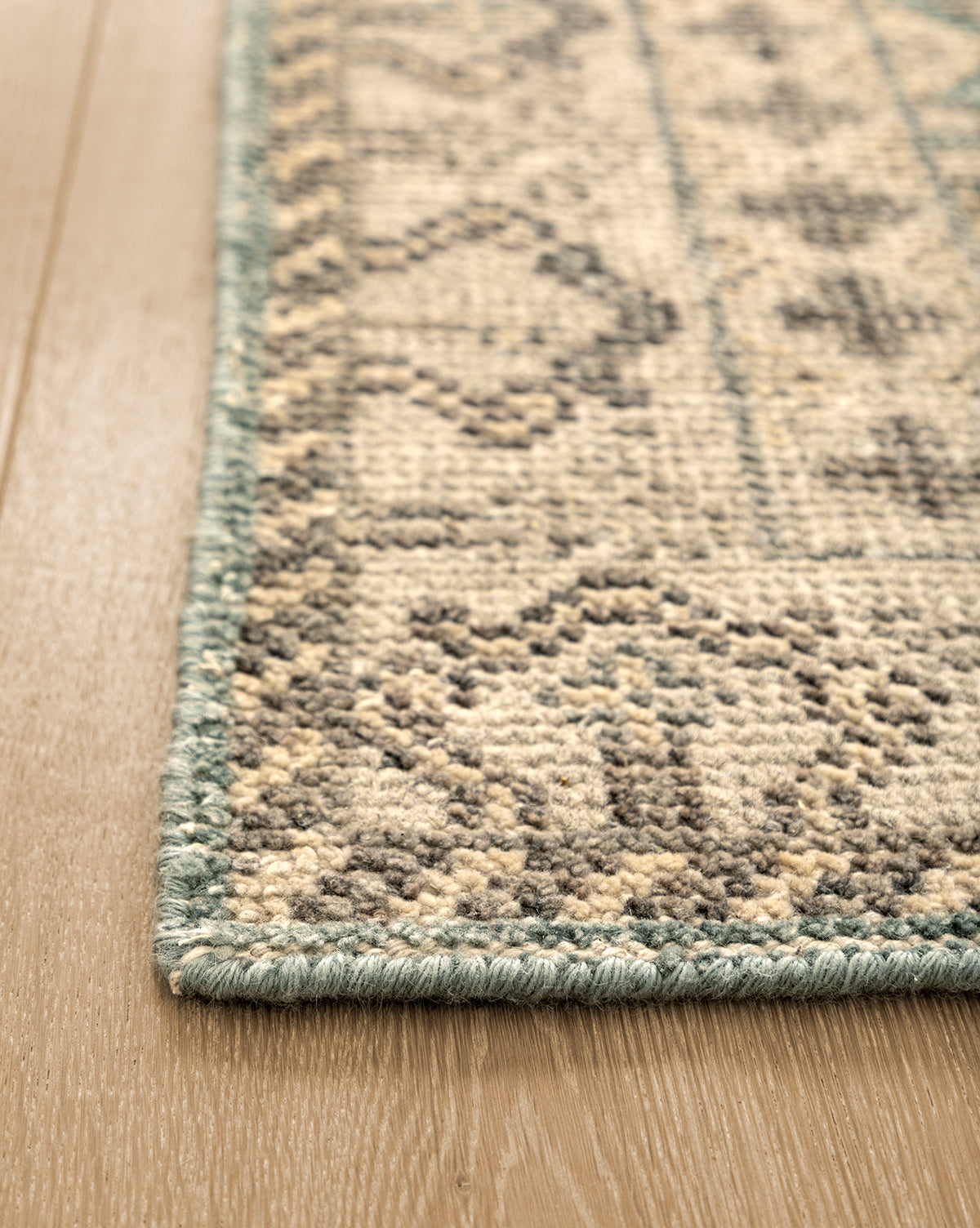 Close-up of the Thames Hand-Knotted Rug, featuring a thick pile and teal border on a light wooden floor. Beige and gray geometric patterns add elegance—ideal for luxury home decor, by McGee & Co.