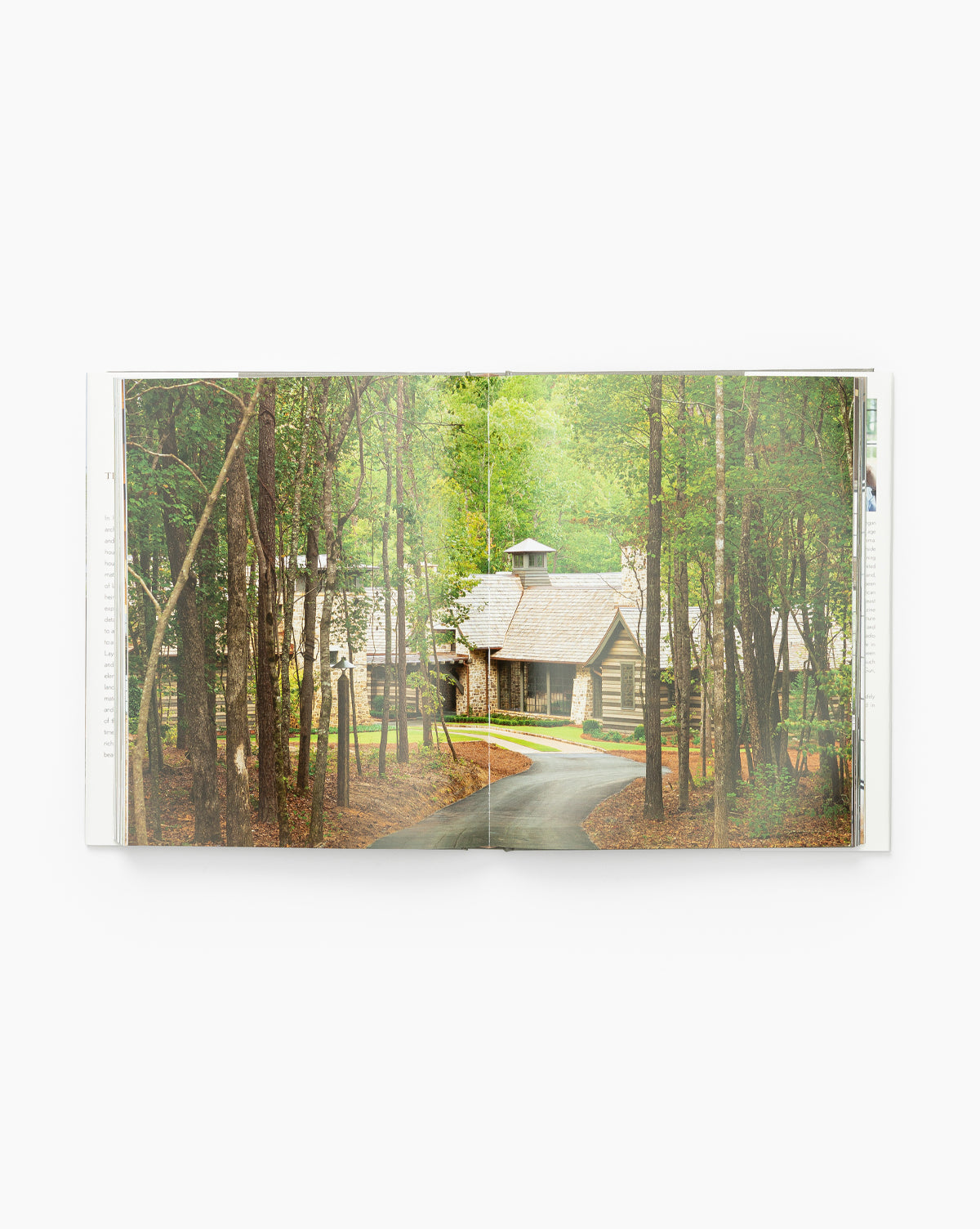 An open copy of The Nature of Home displays a photo of a rustic cabin with a driveway, nestled among tall trees in a lush green forest.