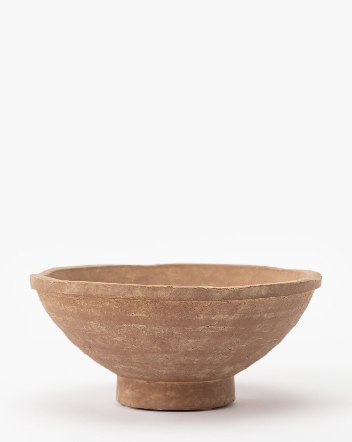 The Theoden Terracotta Bowl is a simple, round, shallow hand-thrown bowl with a small, slightly elevated base. It features a natural earthy brown hue and rough texture, displayed against a plain white background.