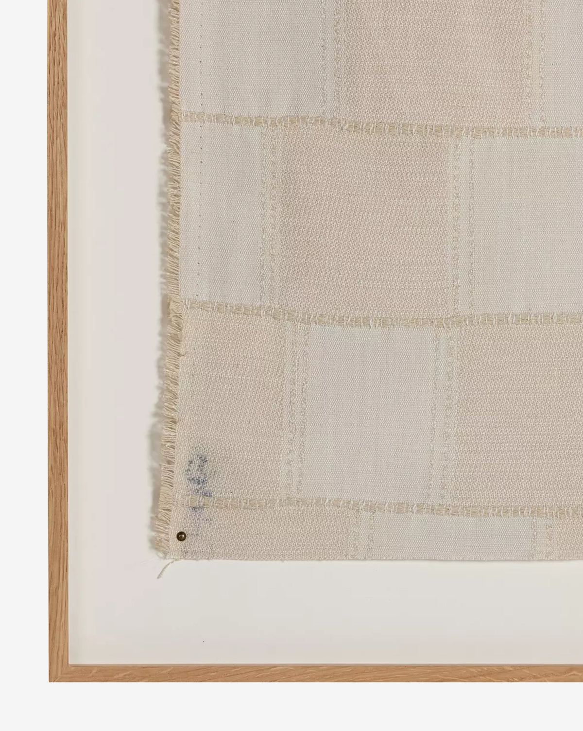 A close-up of the Thomwell Woven Textile shows a beige checkered fabric with frayed edges in a white oak frame, featuring a small blue mark near the bottom left, highlighting this unique textural artwork.