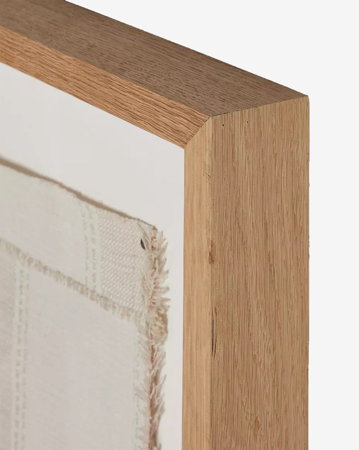 Close-up of the corner of a white oak frame featuring the Thomwell Woven Textile, highlighting detailed wood grain and the artwork’s frayed, textured edge.
