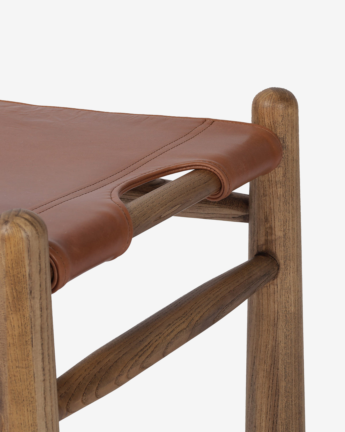 Close-up of the Tierney Ottoman by Four Hands: features a smooth, natural-finish solid wood corner and a brown top grain leather seat with stitched handle detail. McGee & Co.