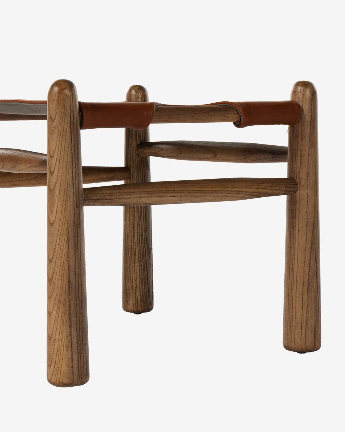 A close-up of the Tierney Ottoman by Four Hands highlights its solid wood frame with rounded legs, top grain leather seat, smooth wood grain, and minimalist design. McGee & Co.