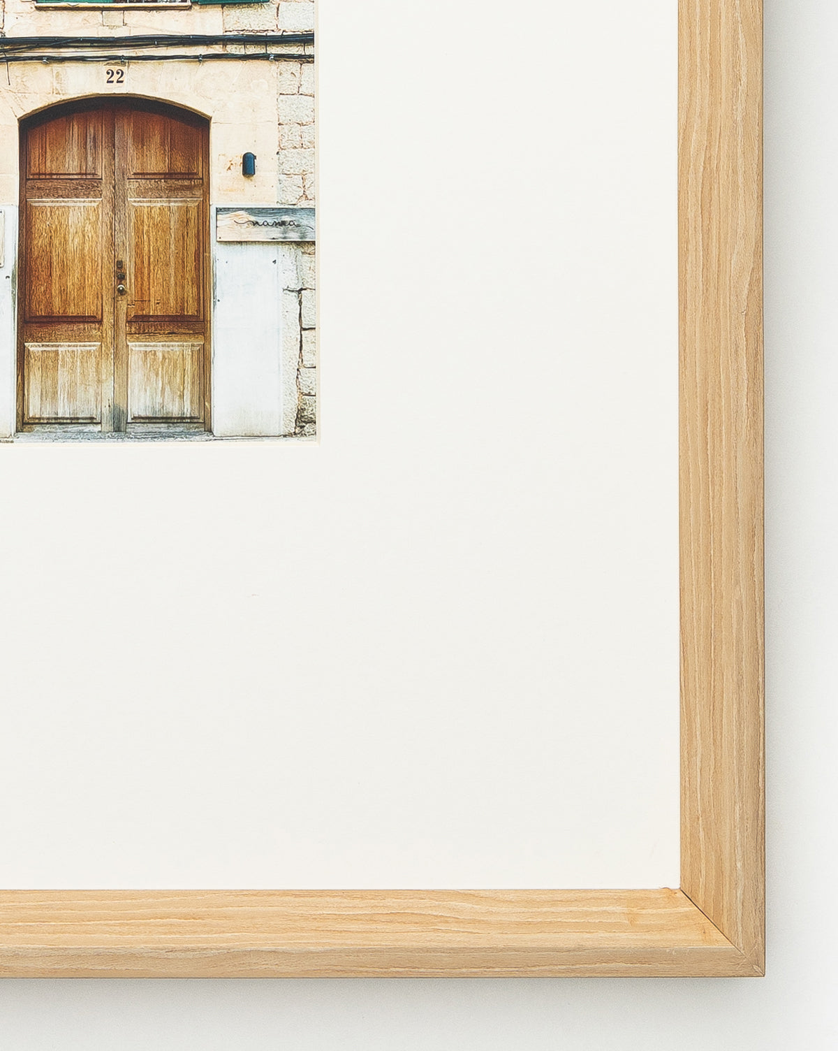 A close-up giclee print titled Town of Deia showcases a rustic double wooden door with the number 22, matted in white and framed in a natural woodgrain frame—ideal for fans of building exterior art.