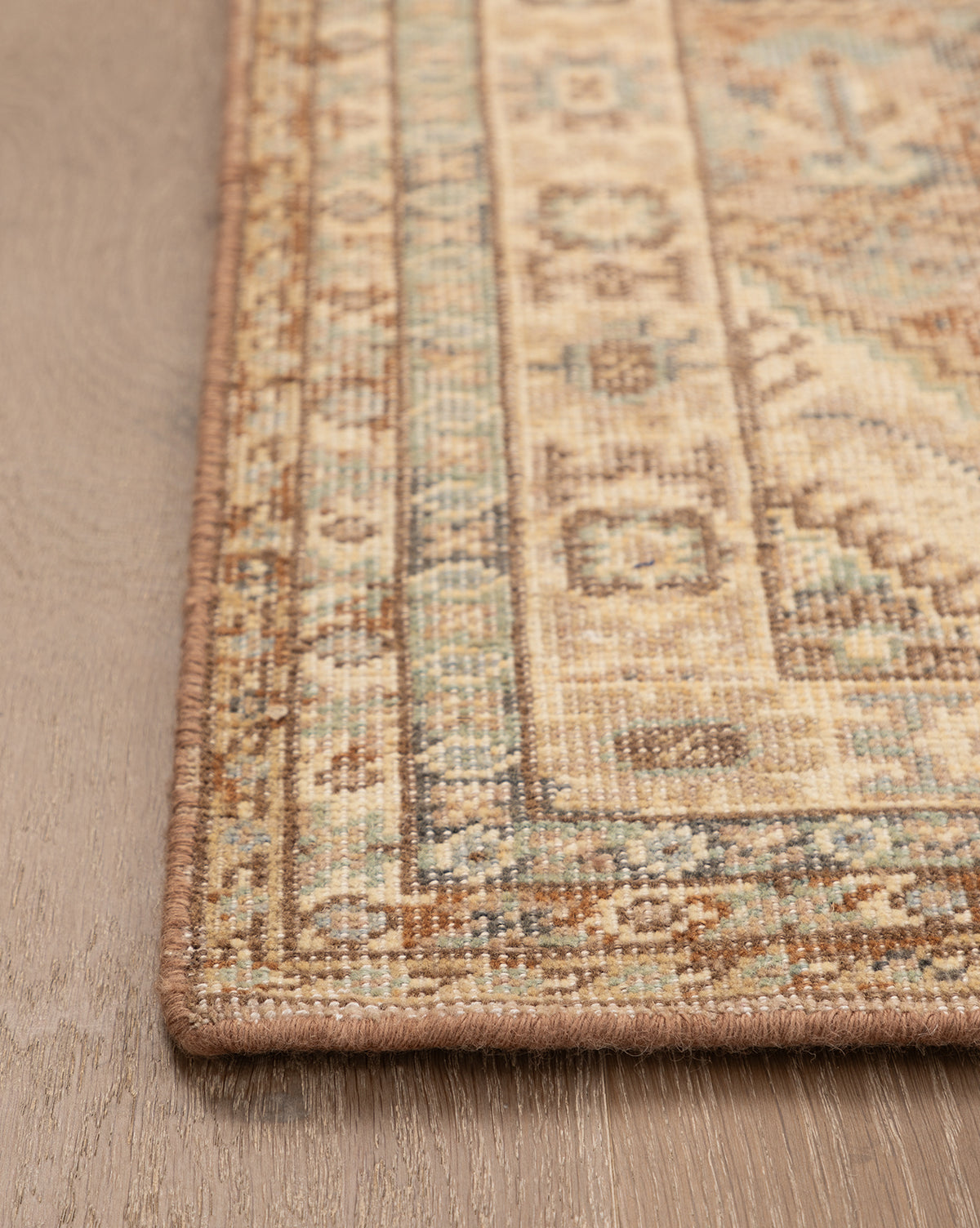 Close-up of the Tulie Hand-Knotted Wool Rug, showcasing its beige, brown, and blue geometric pattern with a detailed traditional border. The rug is displayed on a light wood floor, by McGee & Co.