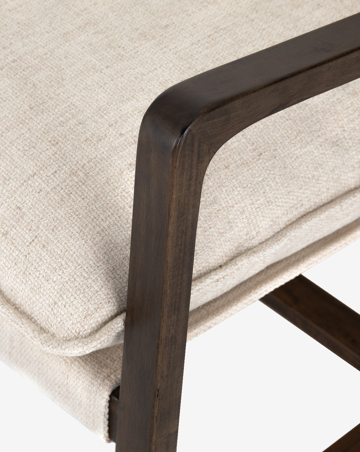 Close-up of the Ura Lounge Chair showcases a cushioned seat in beige high-performance fabric, a dark wooden armrest with smooth, rounded edges, and a solid ash frame that contrasts elegantly with the light upholstery.
