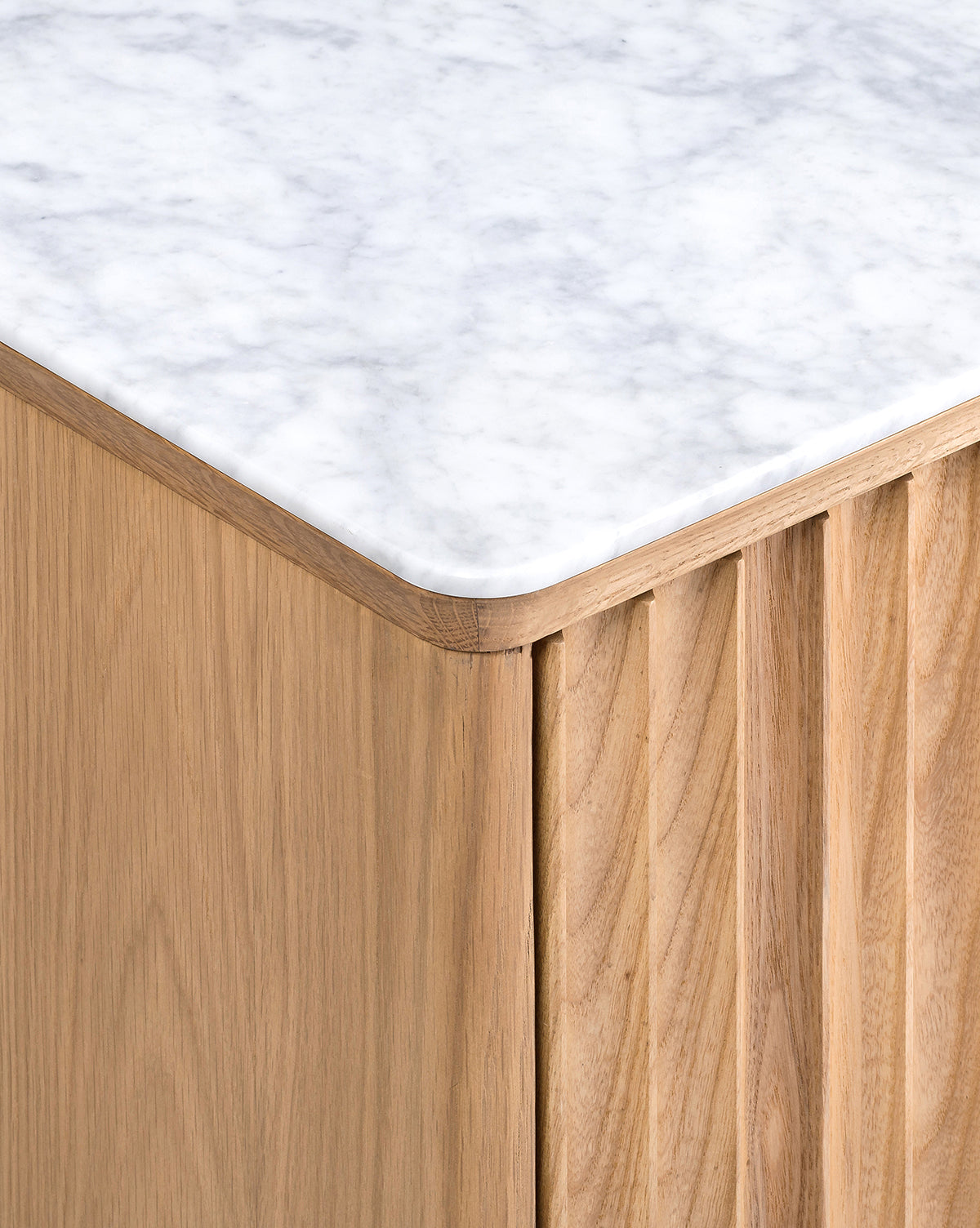 Close-up of a corner of the Vale Sideboard, showcasing its light oak base with vertical grooves, sleek antique brass hardware, and a smooth white marble top accented with grey veining, by McGee & Co.