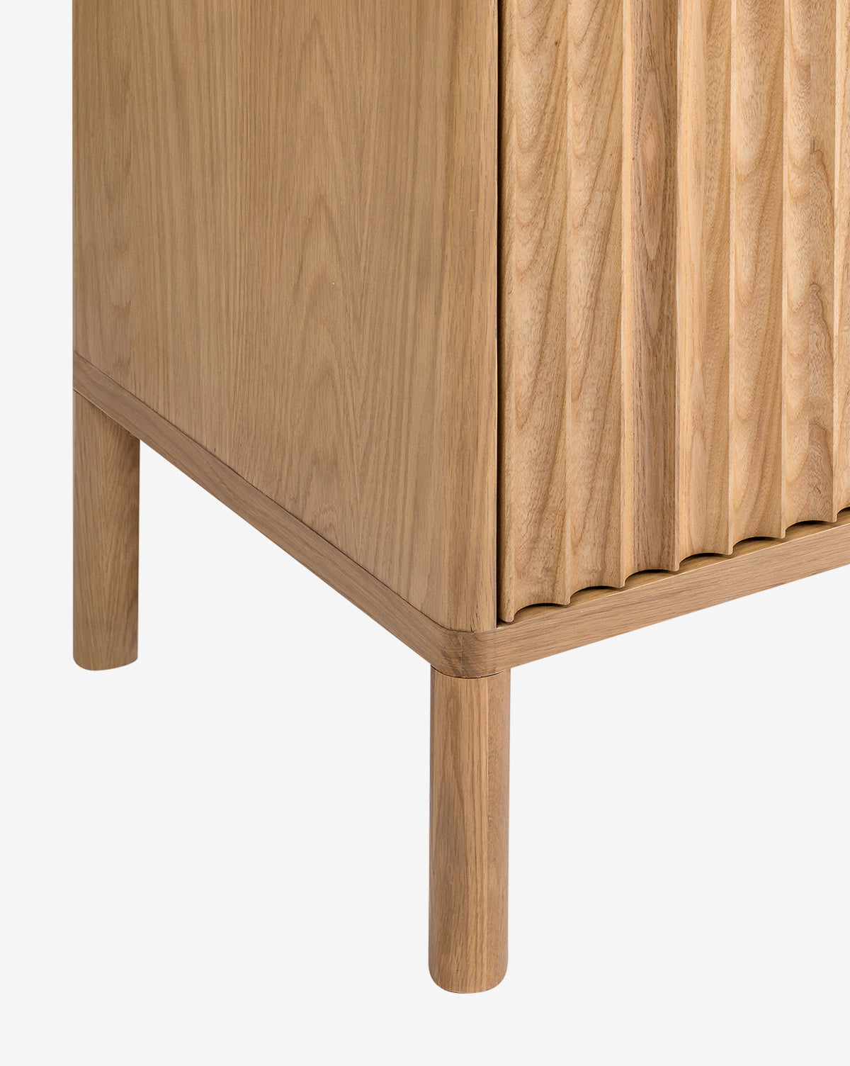 Close-up of the corner of the Vale Sideboard, featuring vertical textured grooves on the oak door, simple cylindrical legs, and a smooth natural finish, by McGee & Co.