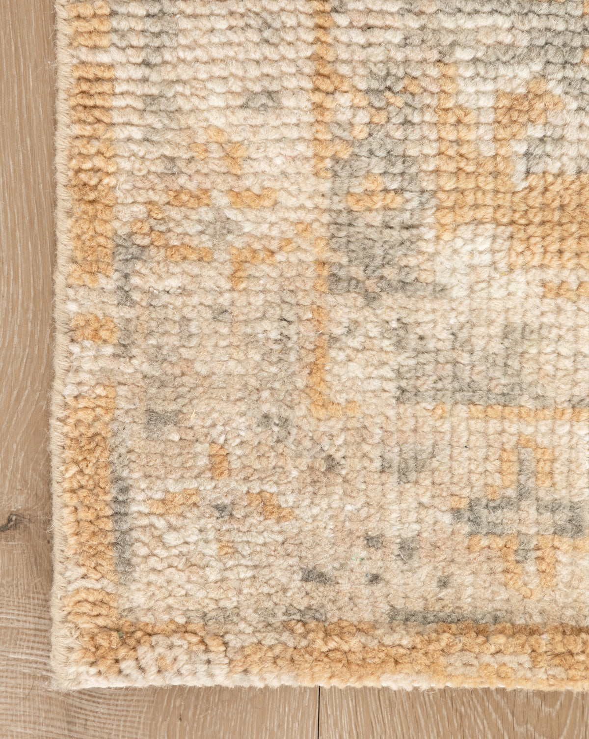 A close-up of the Vanderwood Hand-Knotted Wool Rug shows its thick pile and subtle geometric designs in beige and tan earth tones, lying on a light wooden floor, by McGee & Co.