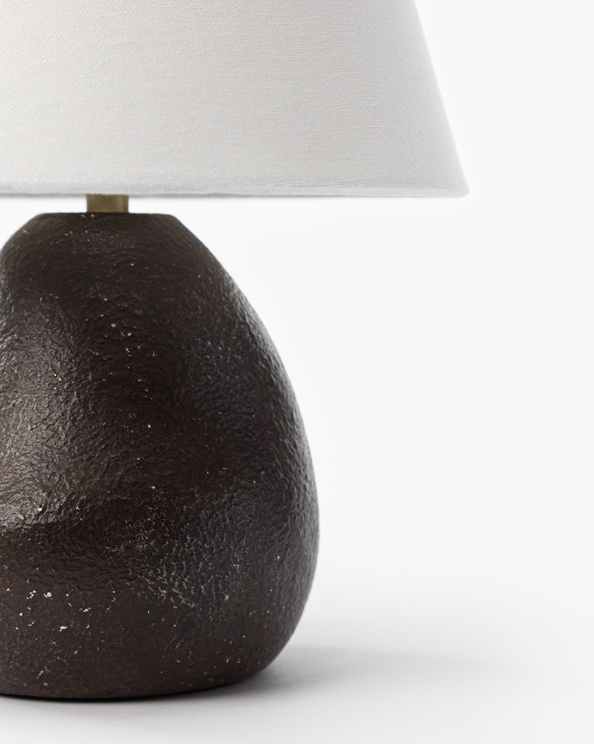 A close-up of the Vedruna Table Lamp with a textured dark brown ceramic base and tapered white shade set against a plain white background, by McGee & Co.