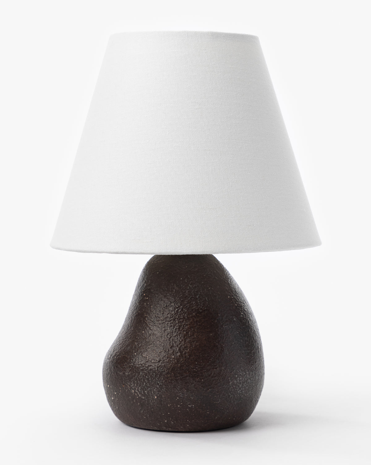 The Makerspalm Vedruna Table Lamp showcases a textured dark brown ceramic base with a large tapered white shade, all presented against a plain white background. McGee & Co.