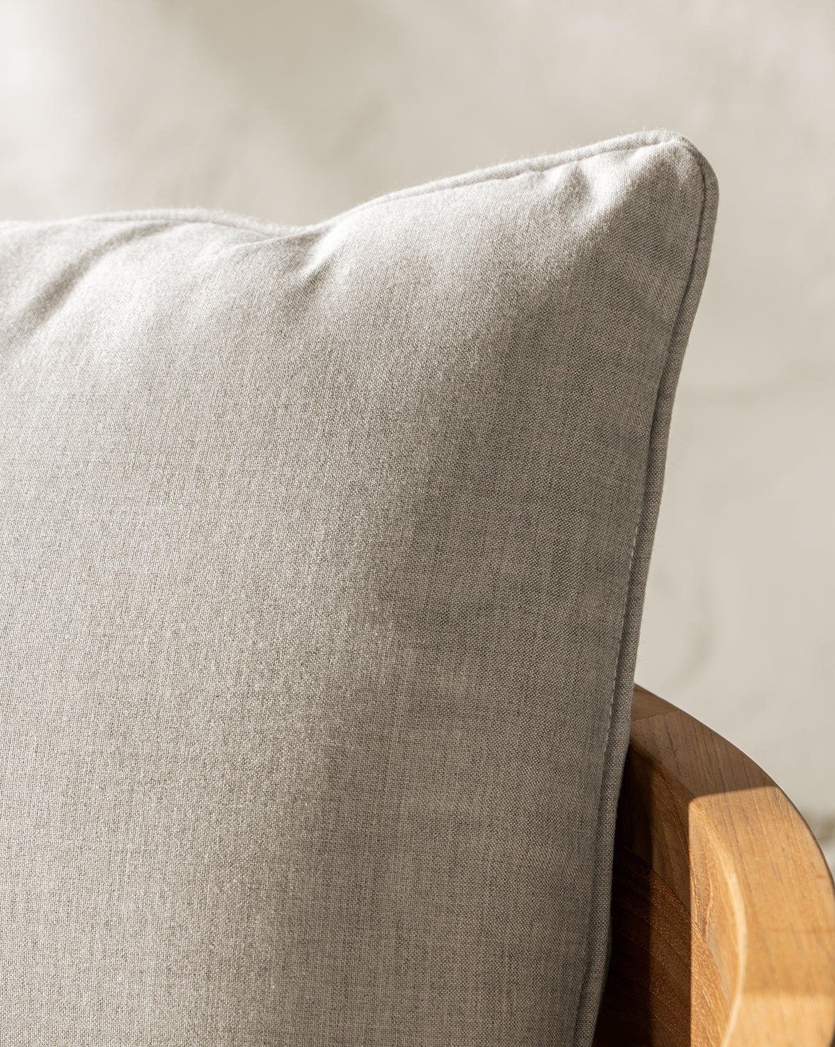 Close-up of a light gray cushion on the wooden arm of the Vento Teak Outdoor Lounge Chair, shown in soft natural light with a blurred white background, by McGee & Co.