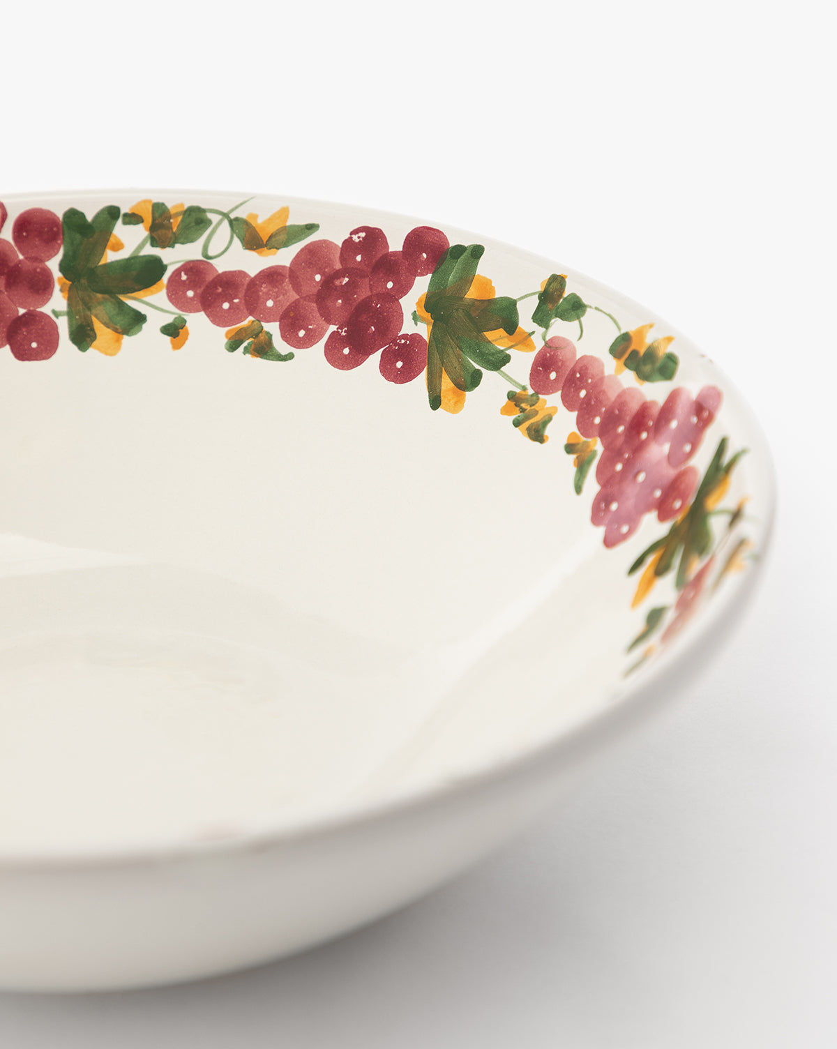 The Vine Large Bowl is a white handmade ceramic piece with a colorful painted rim featuring clusters of red berries, green leaves, and small yellow flowers—a charming addition to any table setting, by McGee & Co.