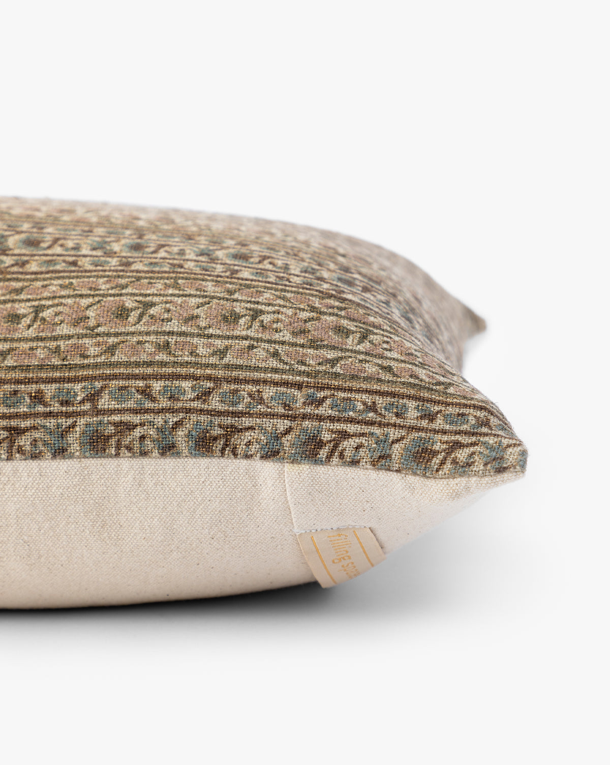 A close-up side view of the Wakefield Pillow Cover showcases its textured, patterned fabric in earthy tones, beige underside, and a small fabric tag on the seam, by McGee & Co.