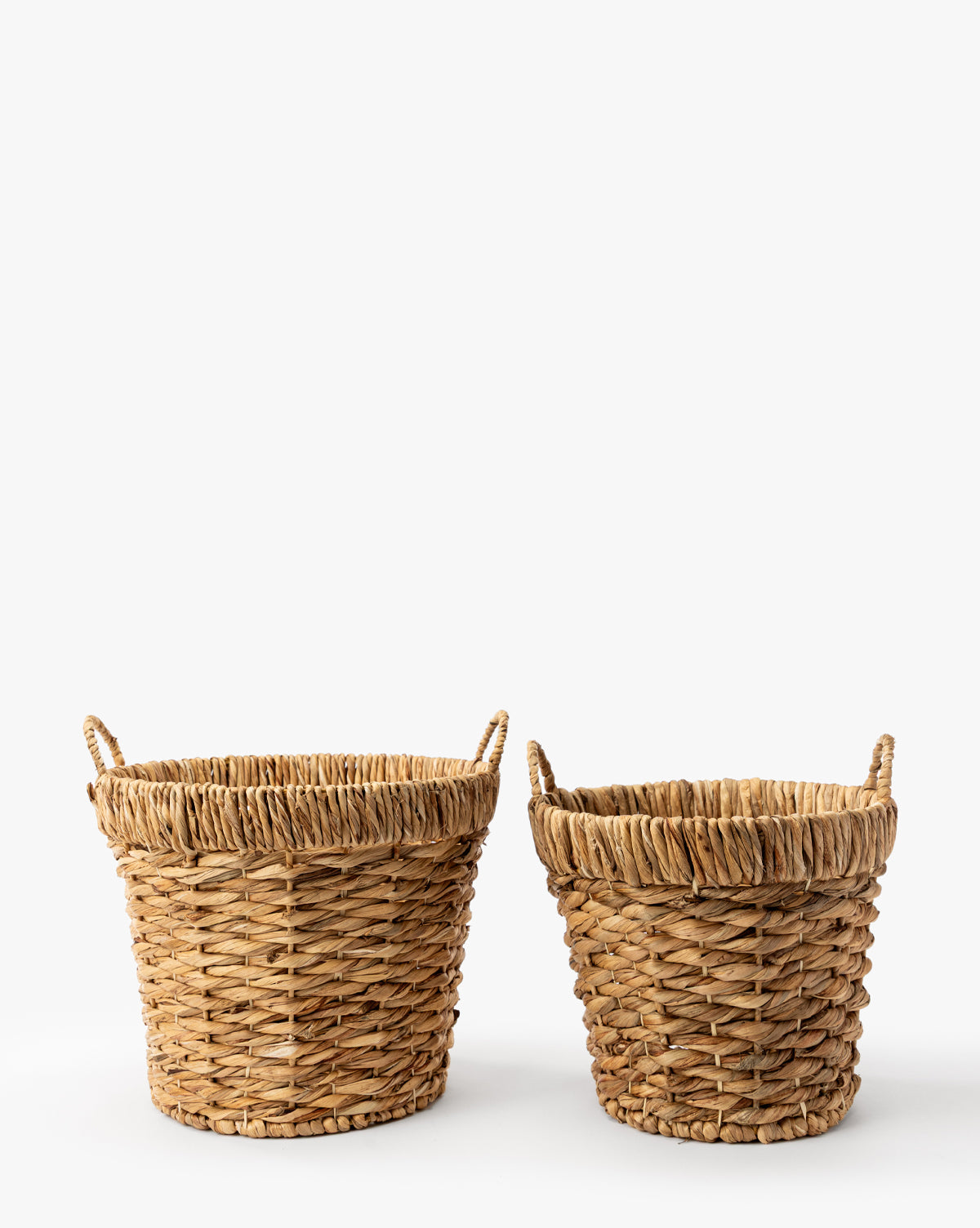 The Water Hyacinth Baskets with Handles (Set of 2) are displayed side by side on a white background, providing stylish decorative storage; the left basket is slightly taller and wider than the right one, by McGee & Co.