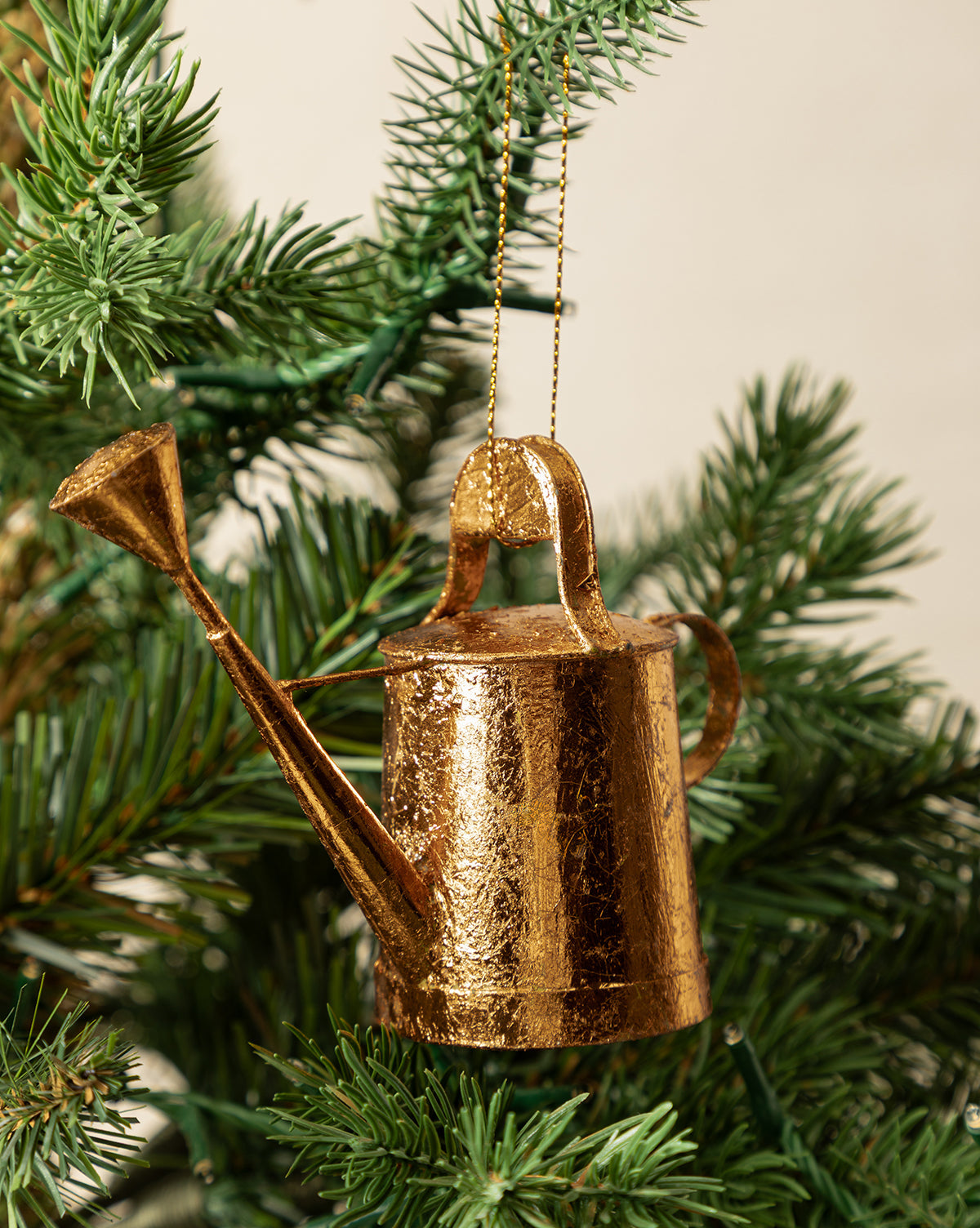The Watering Can Ornament hangs from a green Christmas tree branch, adding unique charm to your festive decor with its copper finish, by McGee & Co.