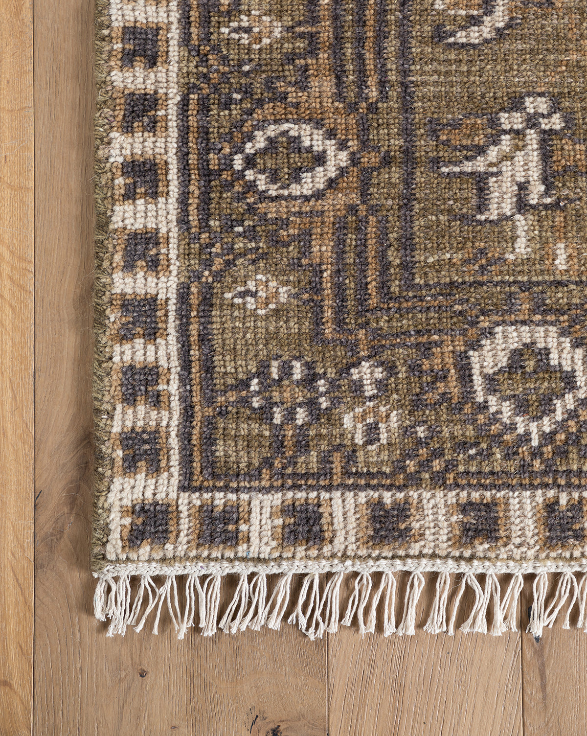 A close-up of the Wayland Hand-Knotted Wool Rug shows its brown, beige, and dark gray geometric and floral patterns with fringe along the edge, displayed on a light wooden floor, by McGee & Co.