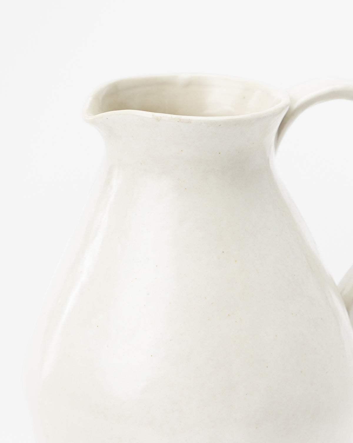 A close-up of the White Ceramic Pitcher, which has a curved spout and handle, a matte off-white finish, and is shown against a plain white background, by McGee & Co.