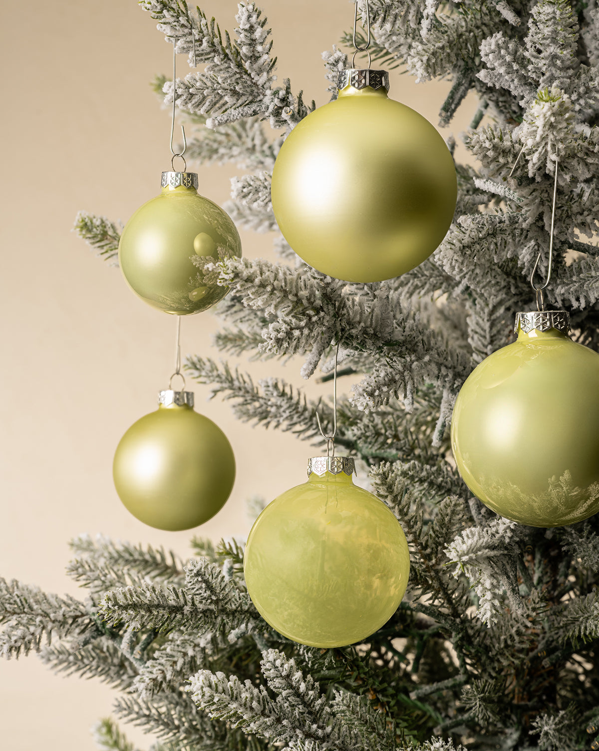 Close-up of a frosted Christmas tree adorned with White Mint Glass Baubles (Set of 21 Assorted), adding elegant holiday charm against a soft beige background, by McGee & Co.