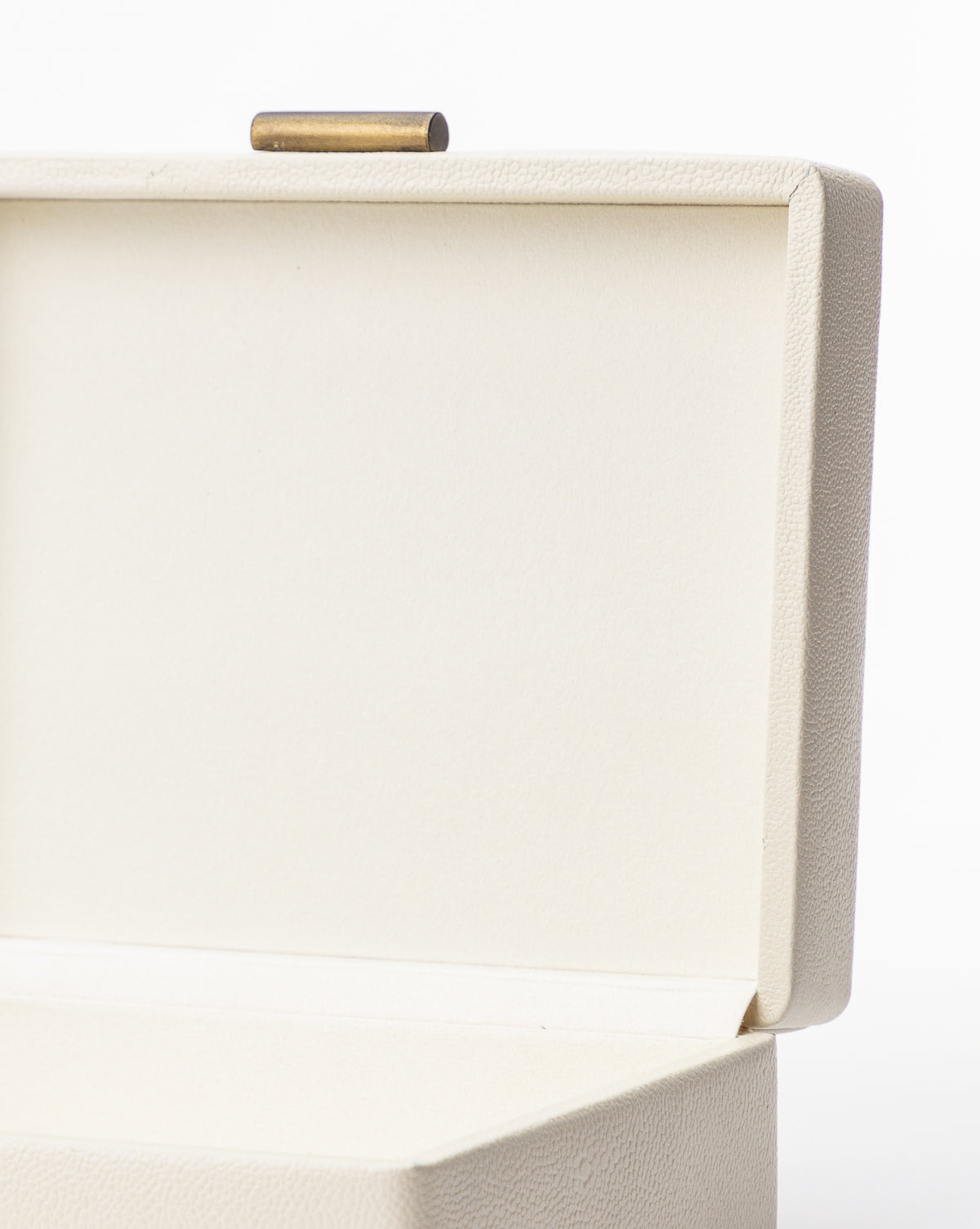 The Cream Shagreen Box, shown open against a white background, features a rectangular shape, textured surface, and a small cylindrical gold clasp at its top edge.