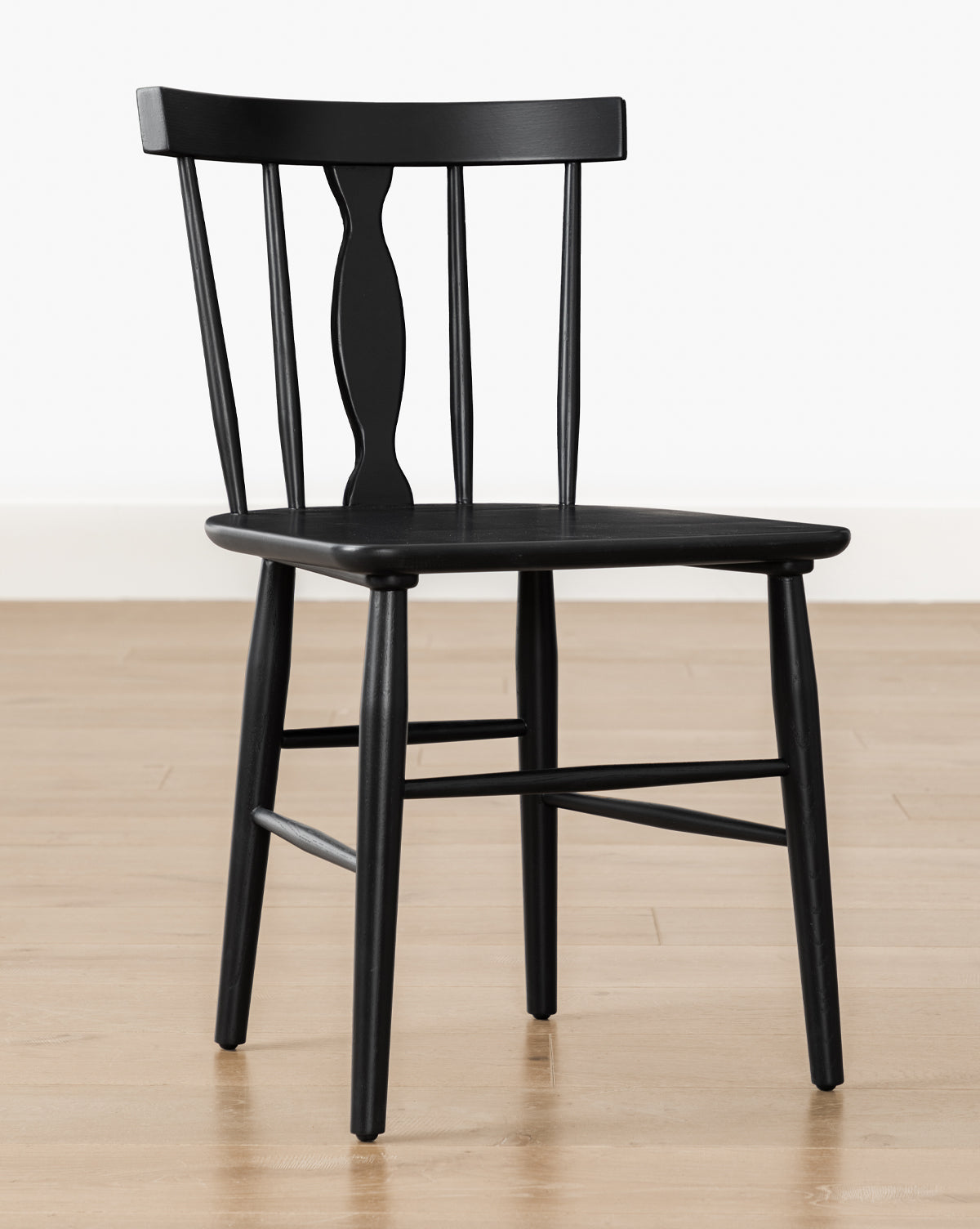 The Whittaker Chair, crafted from solid oak with a curved backrest and vertical spindle supports, stands on a light wooden floor—an ideal accent to enhance any dining space with its timeless design, by McGee & Co.