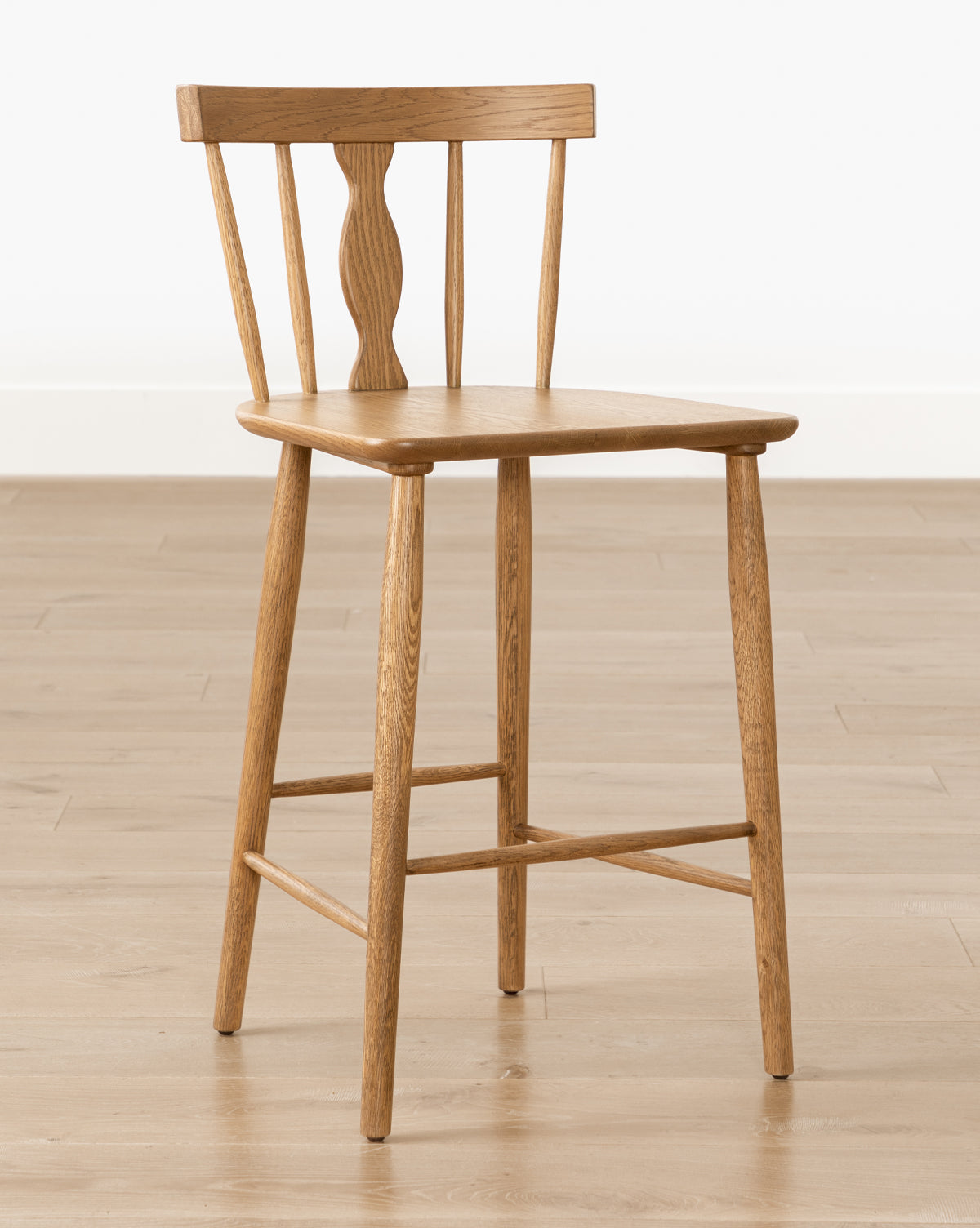 The Whittaker Counter Stool by YANG CHENG WOODEN INDUSTRIES INTERNATIONAL (VIETNAM) CO LTD features a spindle back design and four straight legs, shown on a light wood floor against a plain white wall. McGee & Co.