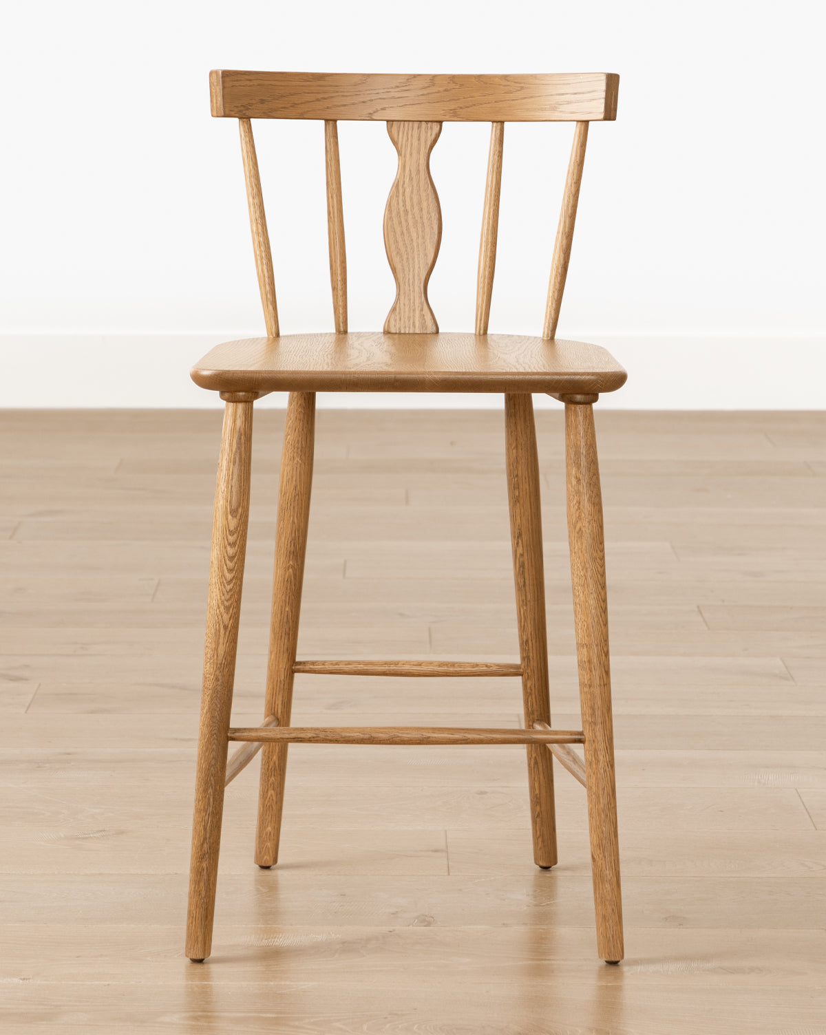 A Whittaker Counter Stool by YANG CHENG WOODEN INDUSTRIES INTERNATIONAL (VIETNAM) CO LTD, with a solid oak finish and spindle back design, stands on a light wood floor against a plain white background. McGee & Co.