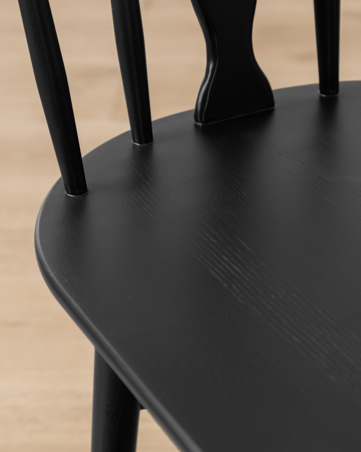 Close-up of the Whittaker Chair, showing vertical backrest slats and a smooth, rounded solid oak seat on a light wood floor—ideal for modern dining spaces, by McGee & Co.